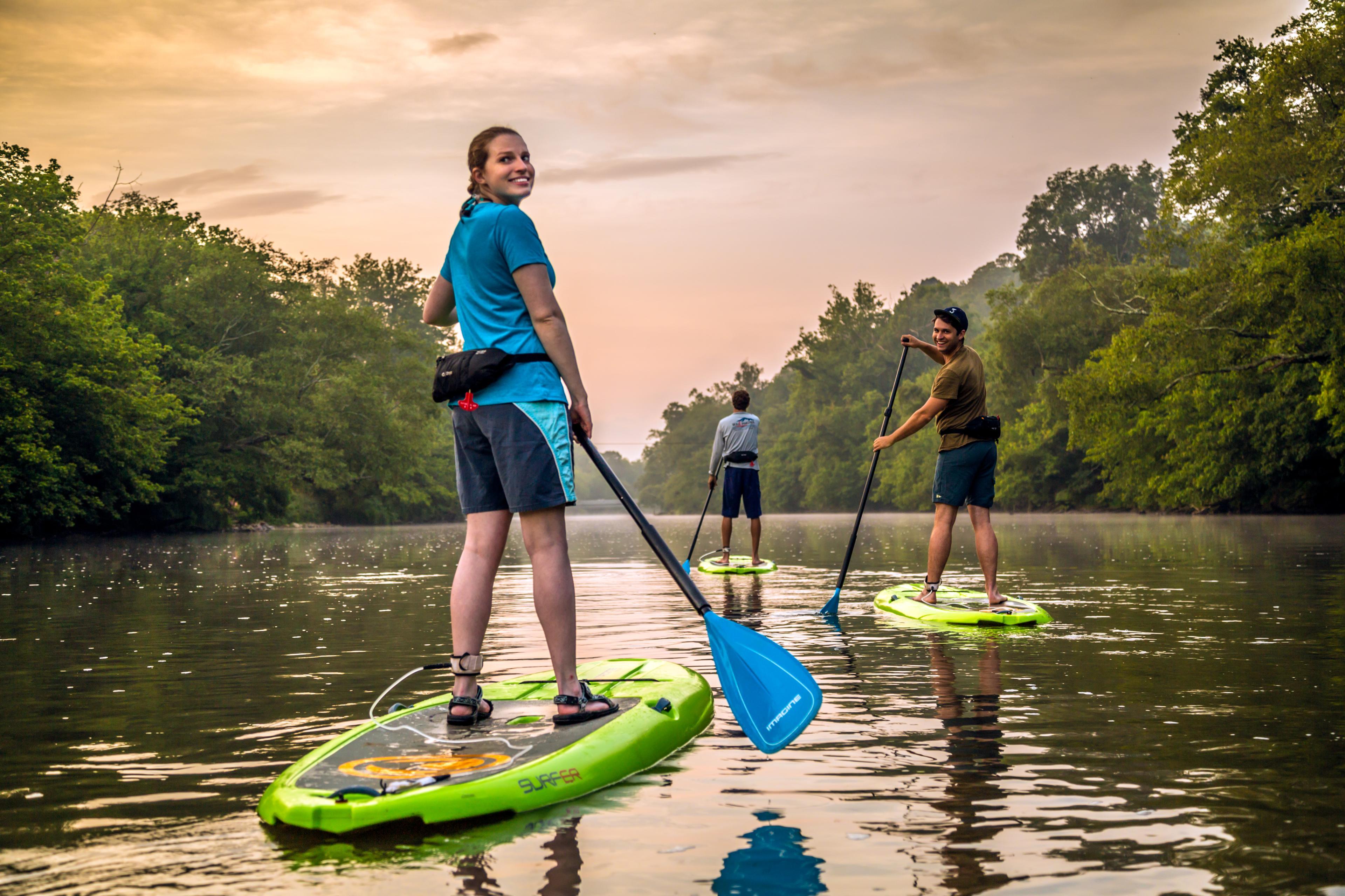 Three people paddle down an Asheville waterway at sunset