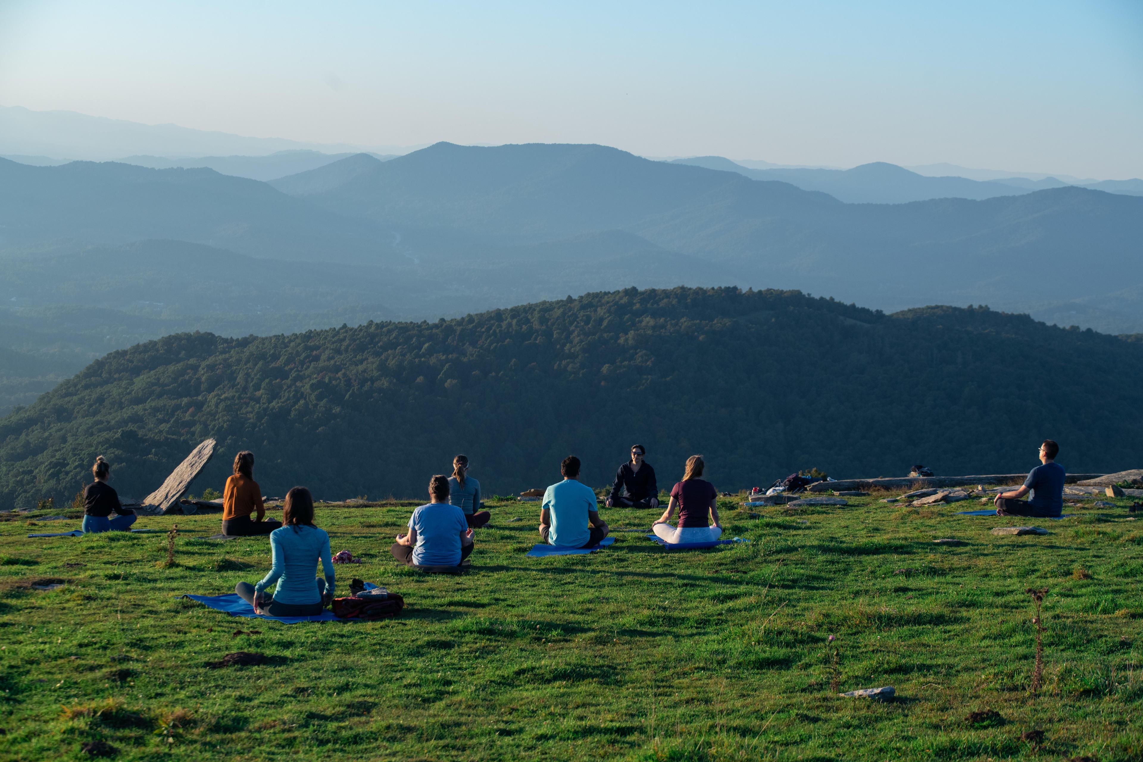 A group of people doing yoga in a mountain field along Bearwallow Trail in Asheville