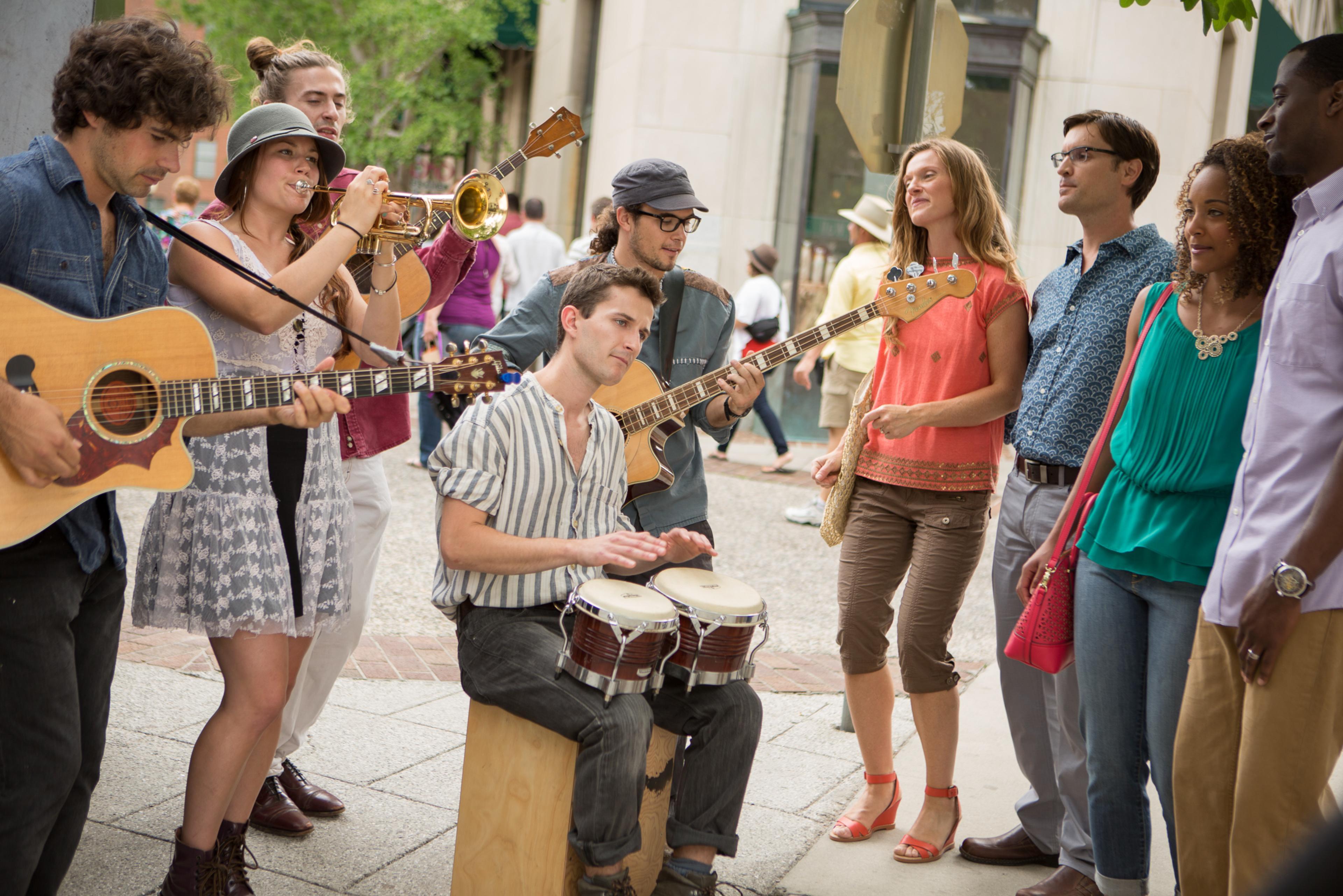 A busker sits amid other musicians and an audience playing the bongos in Asheville