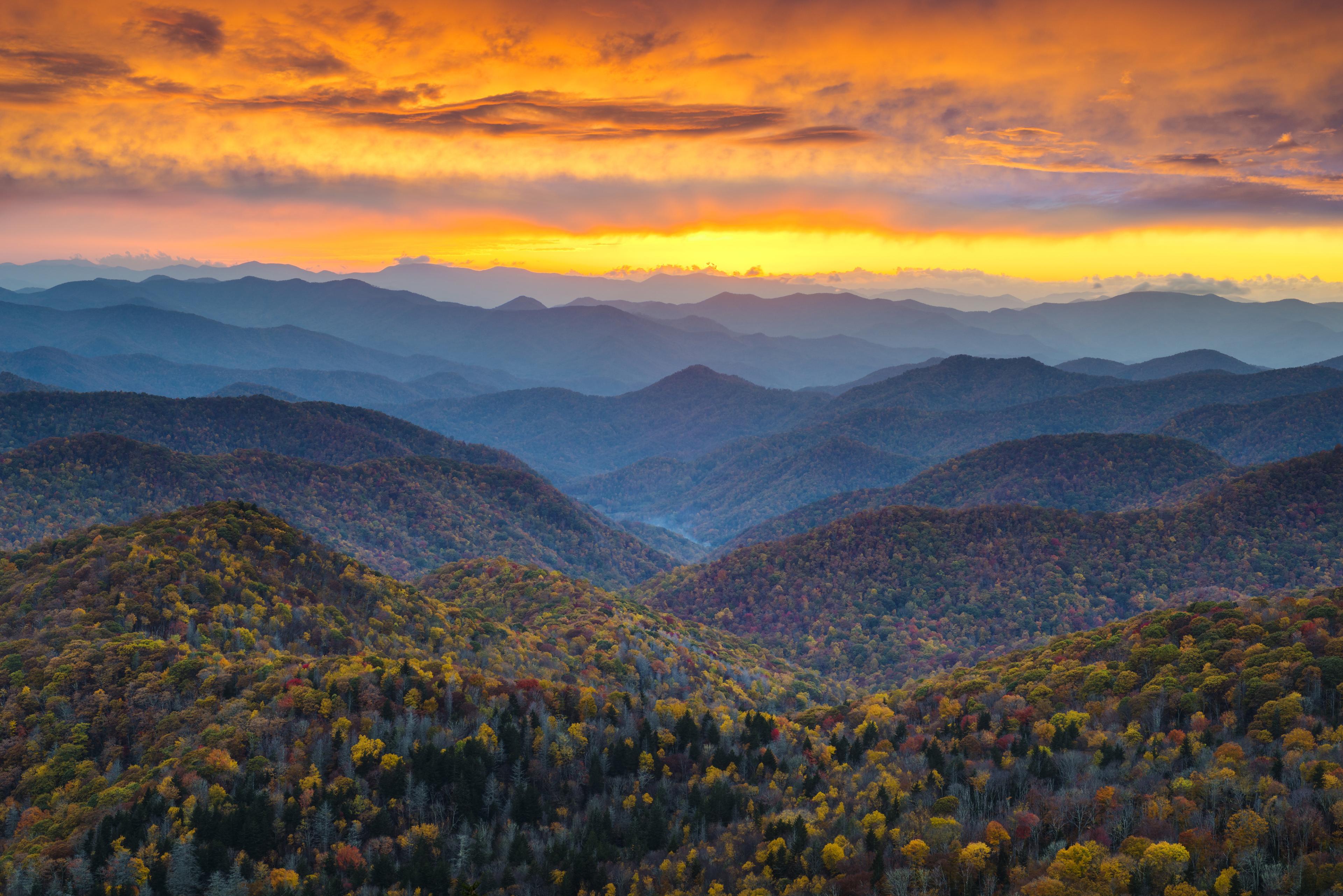 Blue mountains below a sun-streaked orange sky in Asheville