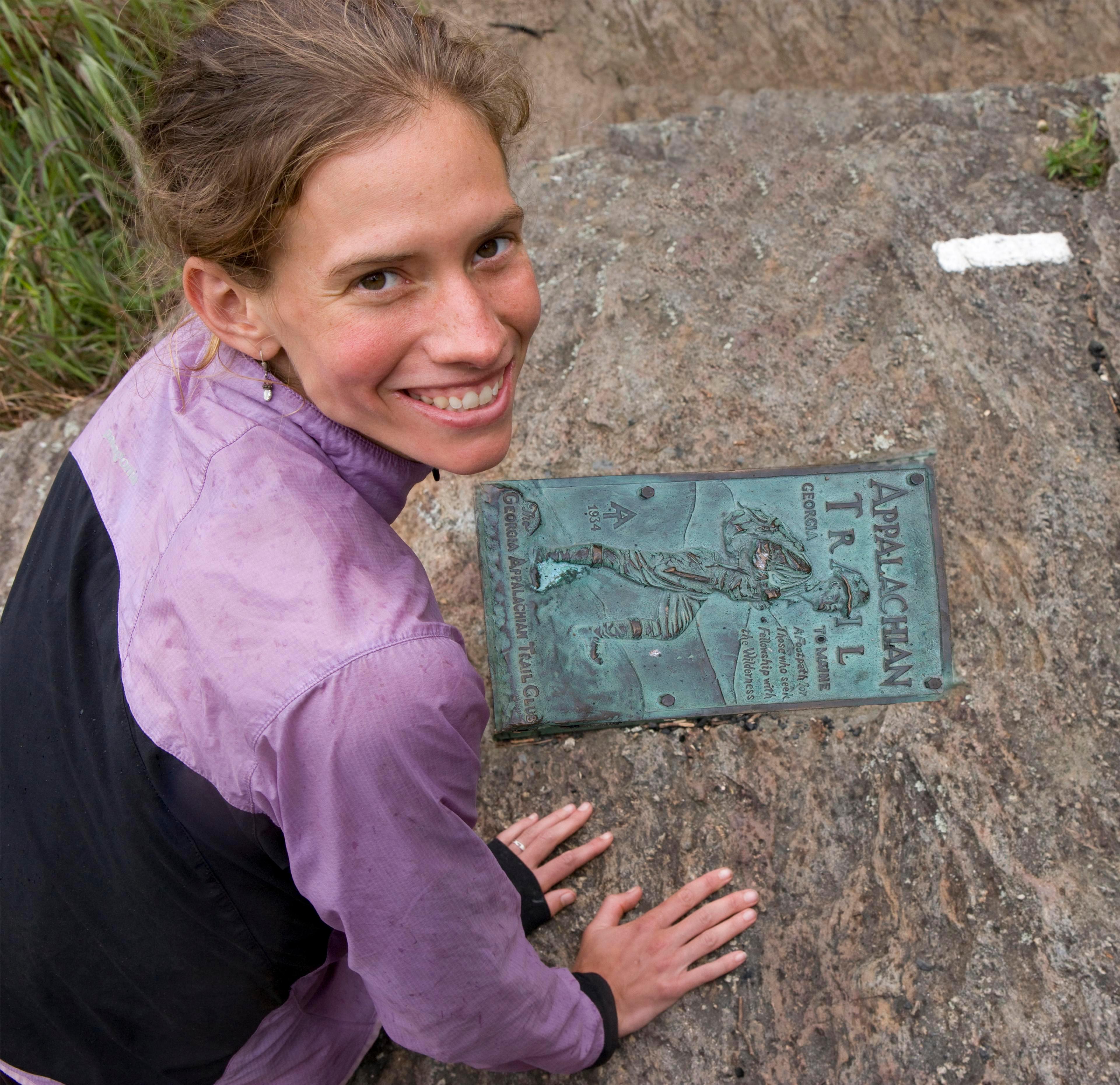 A hiker poses next to an Appalachian Trail plaque