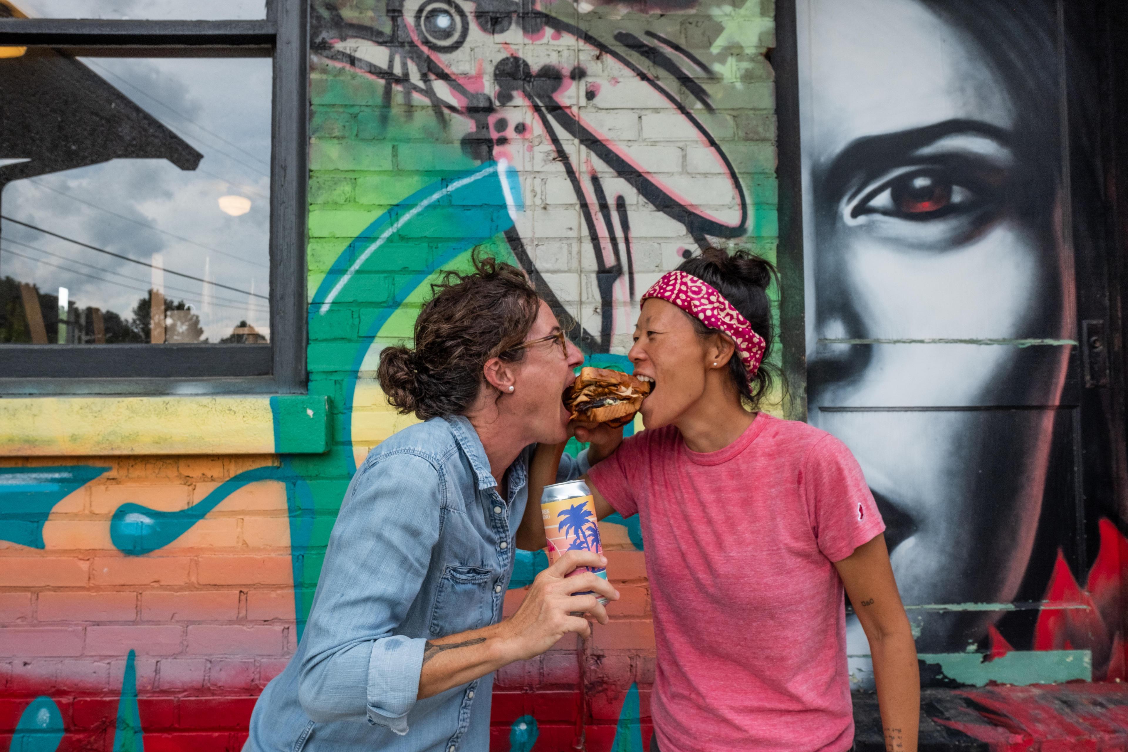 Two people try to take a bite of the same sandwich in Asheville's River Arts District