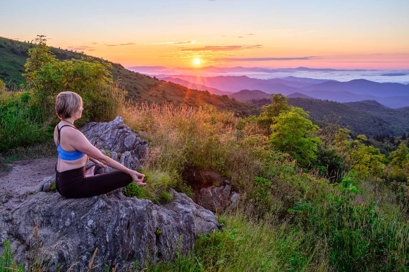 A woman does yoga as the sun rises over Ashville's mountains