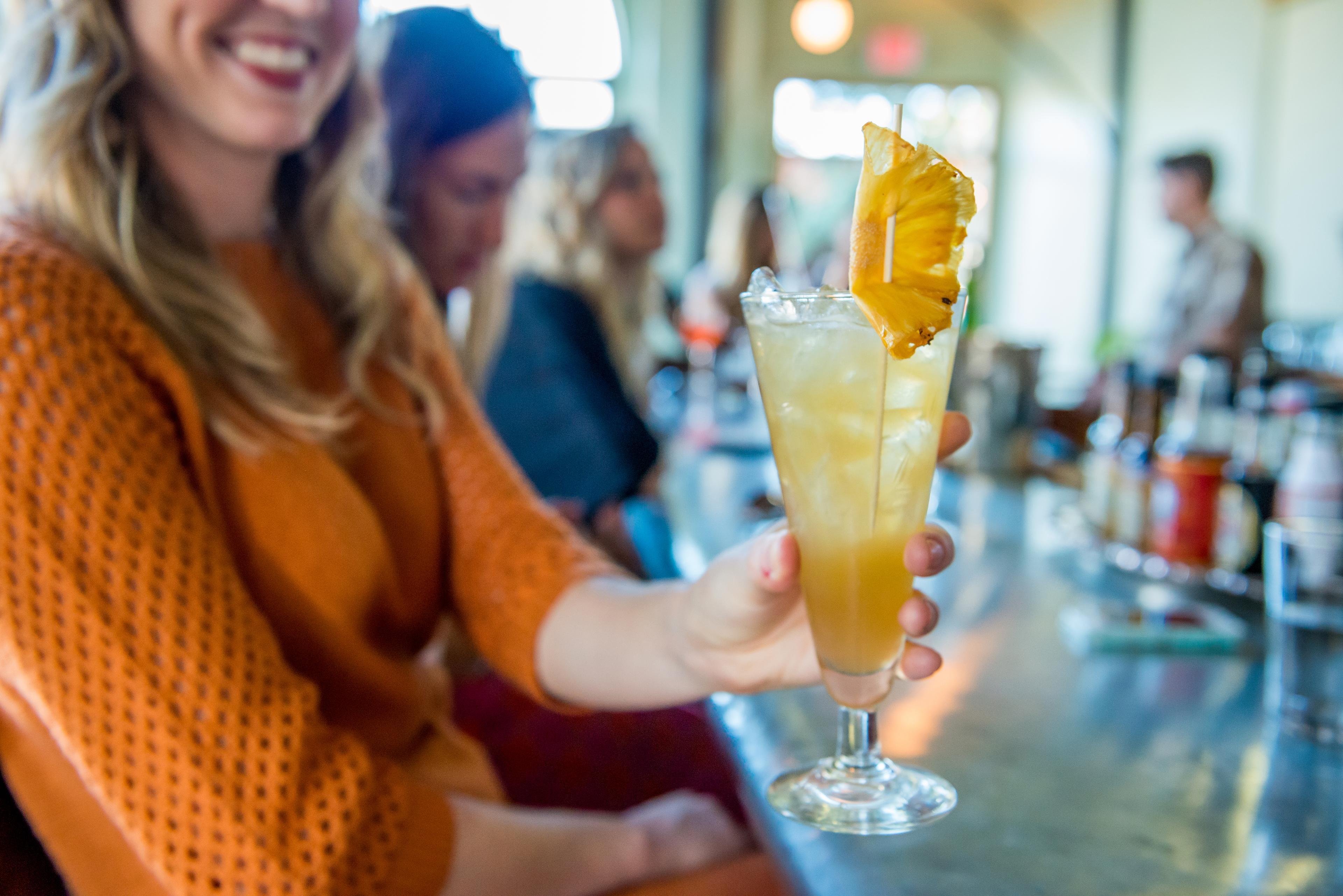 A person at a bar holds an orange-y cocktail up to the camera in Asheville