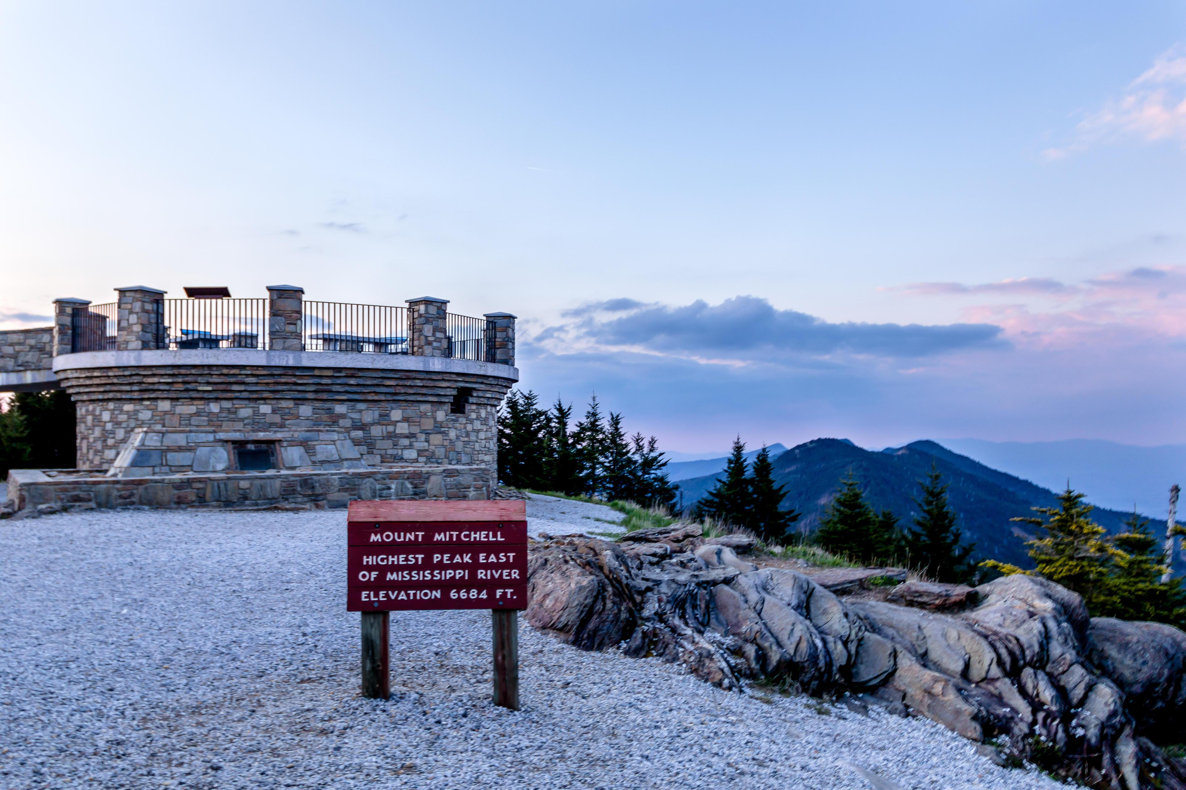 a sign read "Mt. Mitchell" at sunset, overlooking beautiful mountains